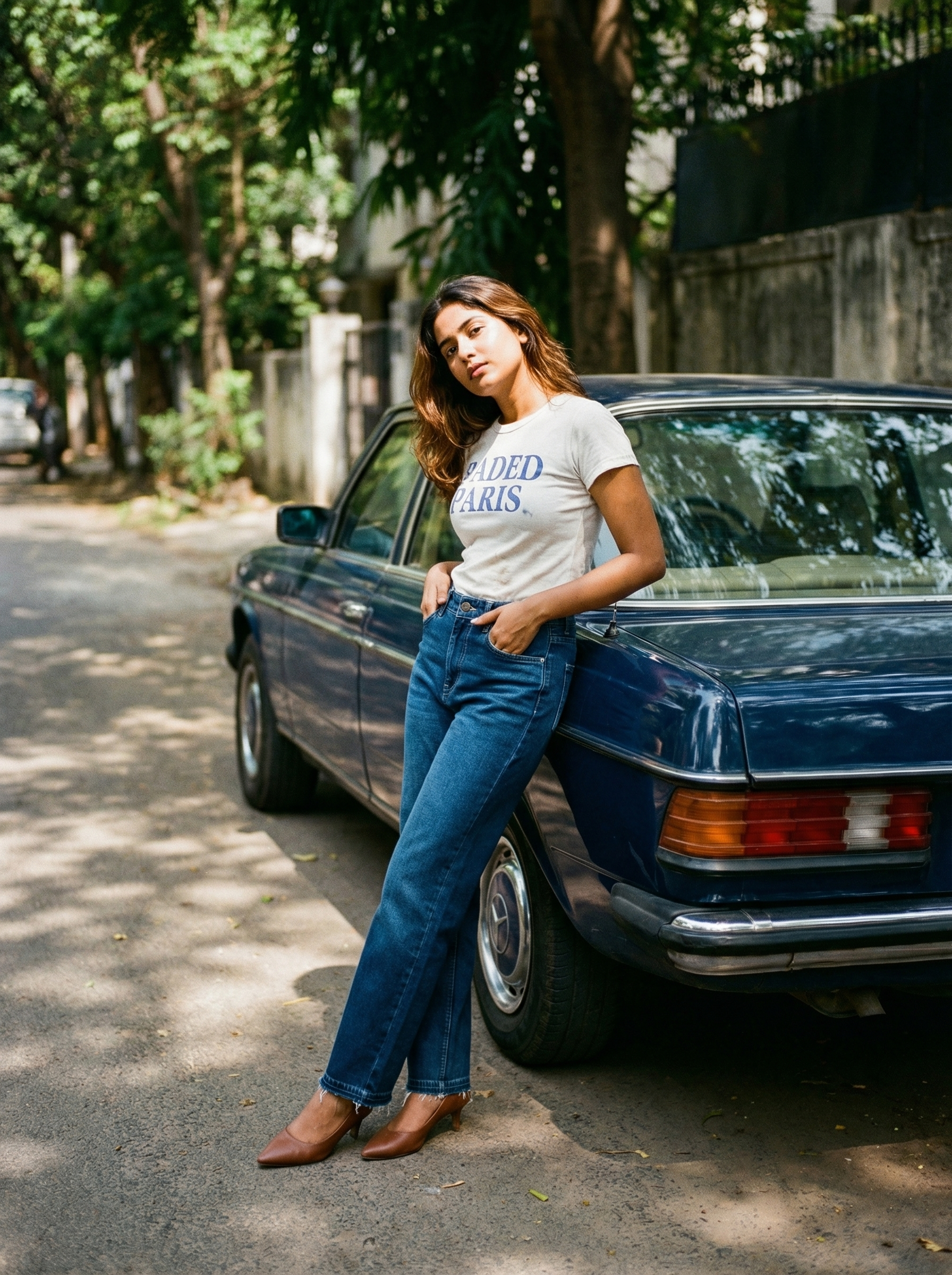Woman leaning against a vintage blue car on a tree-lined street wearing NOIR Core indigo