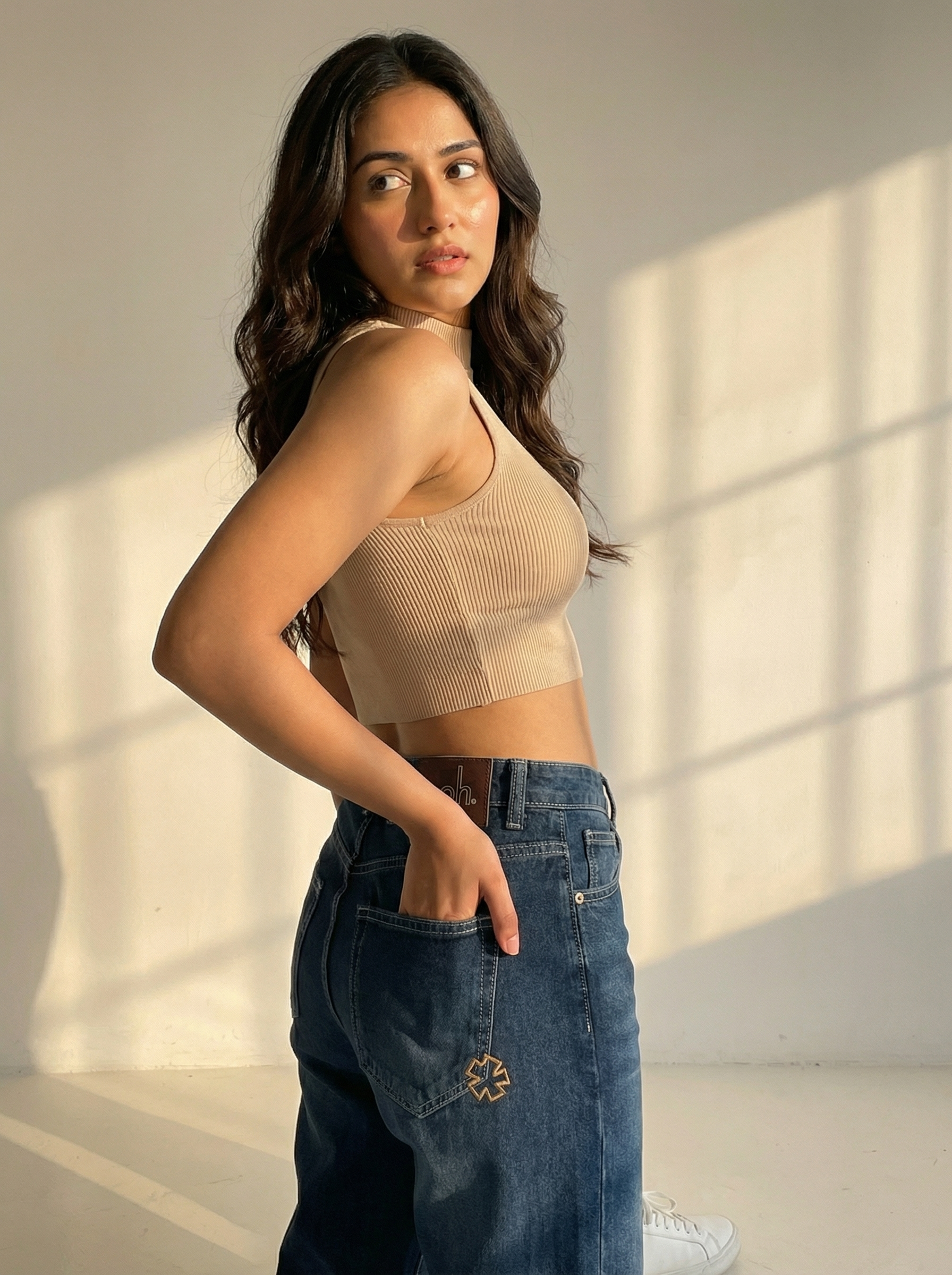 Woman wearing a beige top and NOIR Core indigo jeans standing in a softly lit room.
