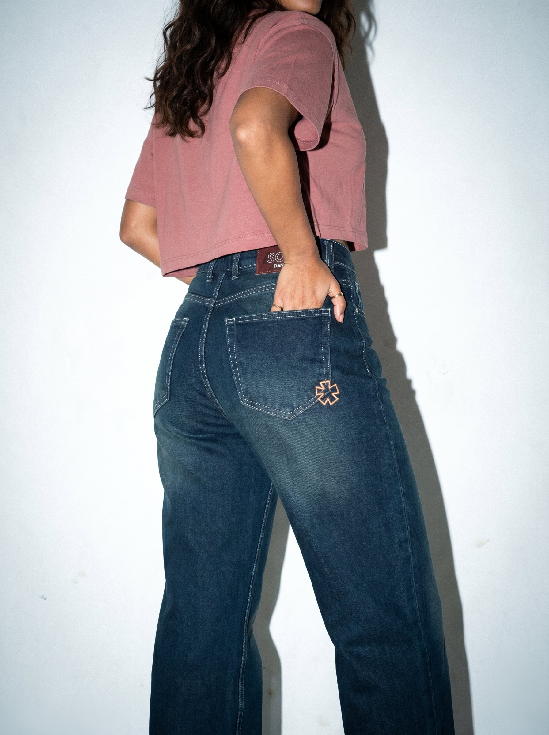 Person wearing Noir Afterlight Indigo jeans and a pink crop top against a white background