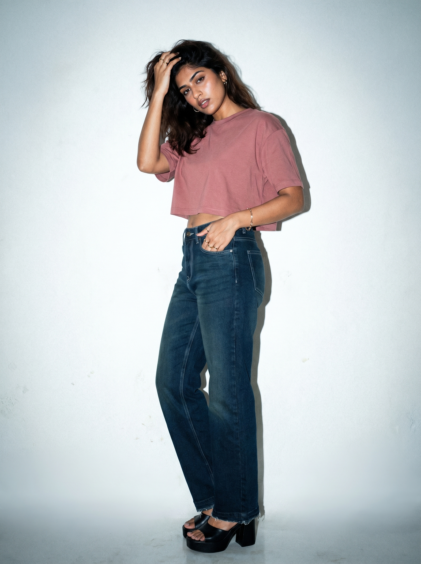 Woman wearing a pink crop top and Noir Afterlight Indigo jeans against a white background