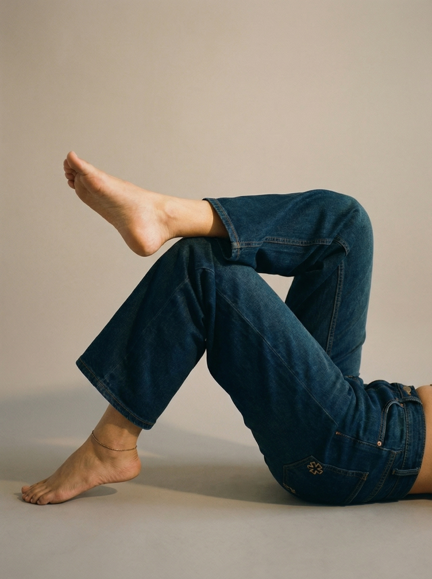 Person wearing Nova Afterlight Indigo jeans sitting on a beige surface with a neutral background