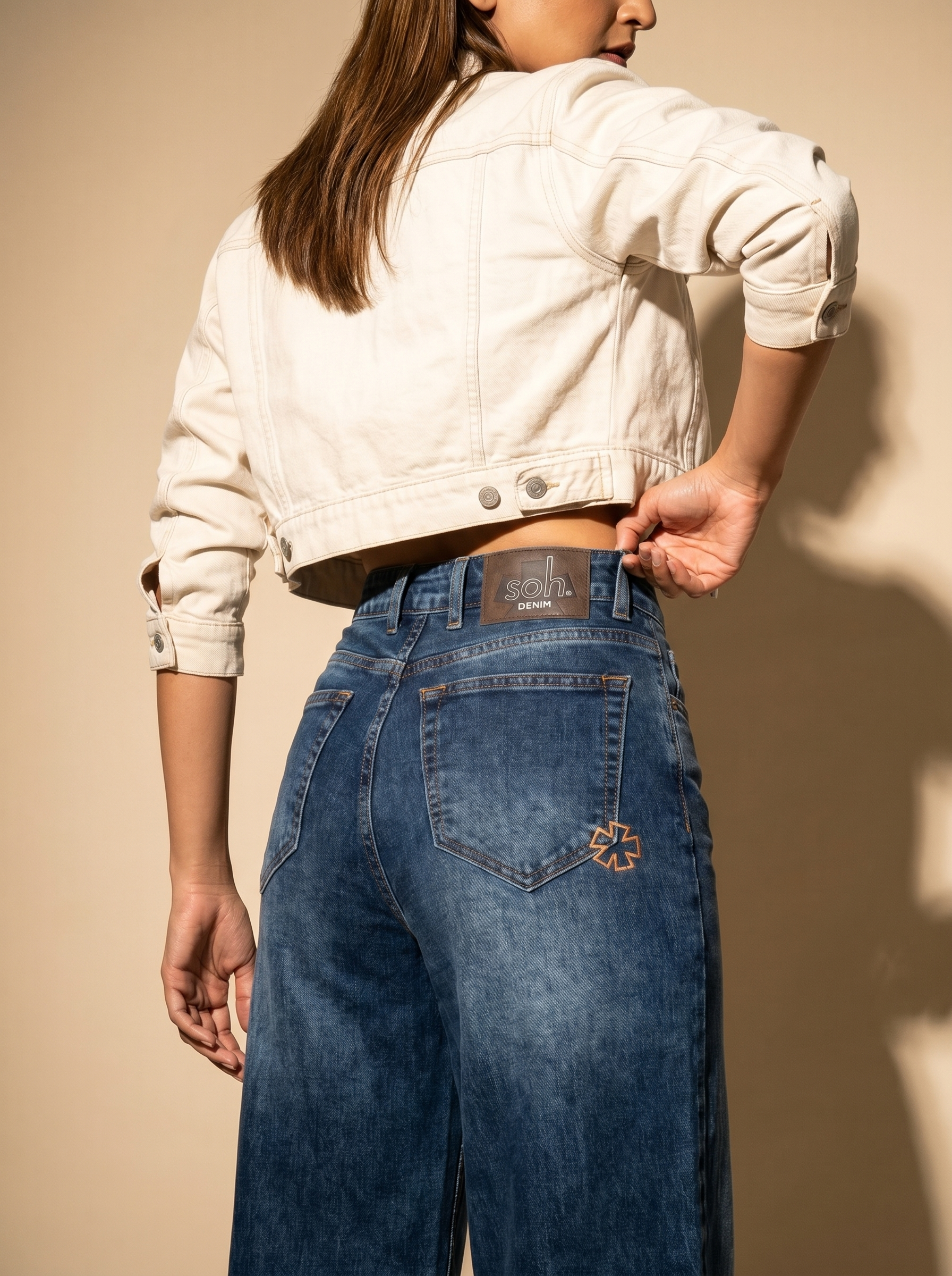 Person wearing a white jacket and blue jeans against a beige background