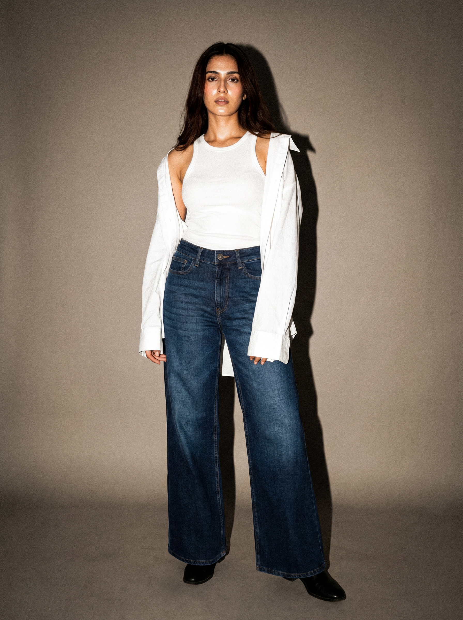 Woman wearing a white top and blue jeans against a plain background