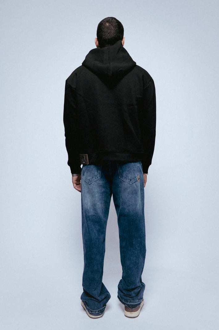 Person wearing a SOH Hoodie Error 01 and blue jeans standing against a light gray background