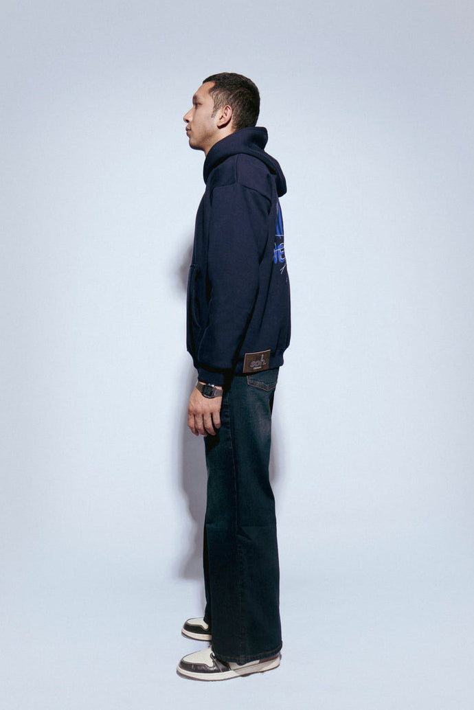 Man wearing a SOH Hoodie Error 02 and jeans standing against a white wall
