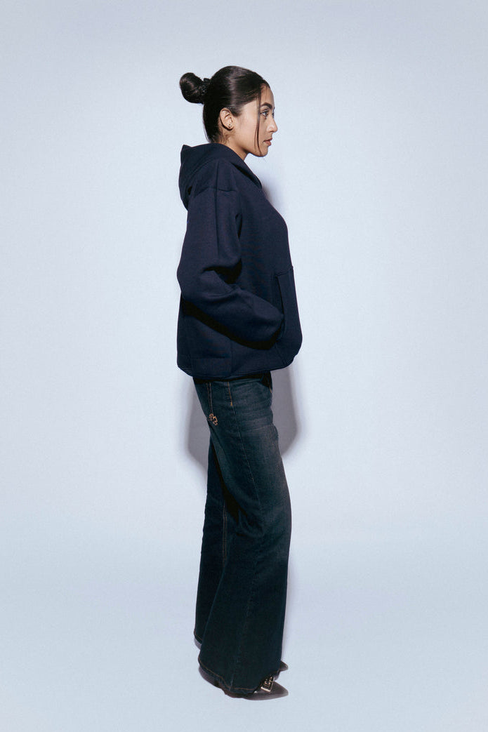 Woman wearing a SOH Hoodie Error 02 and SOH jeans standing against a white background