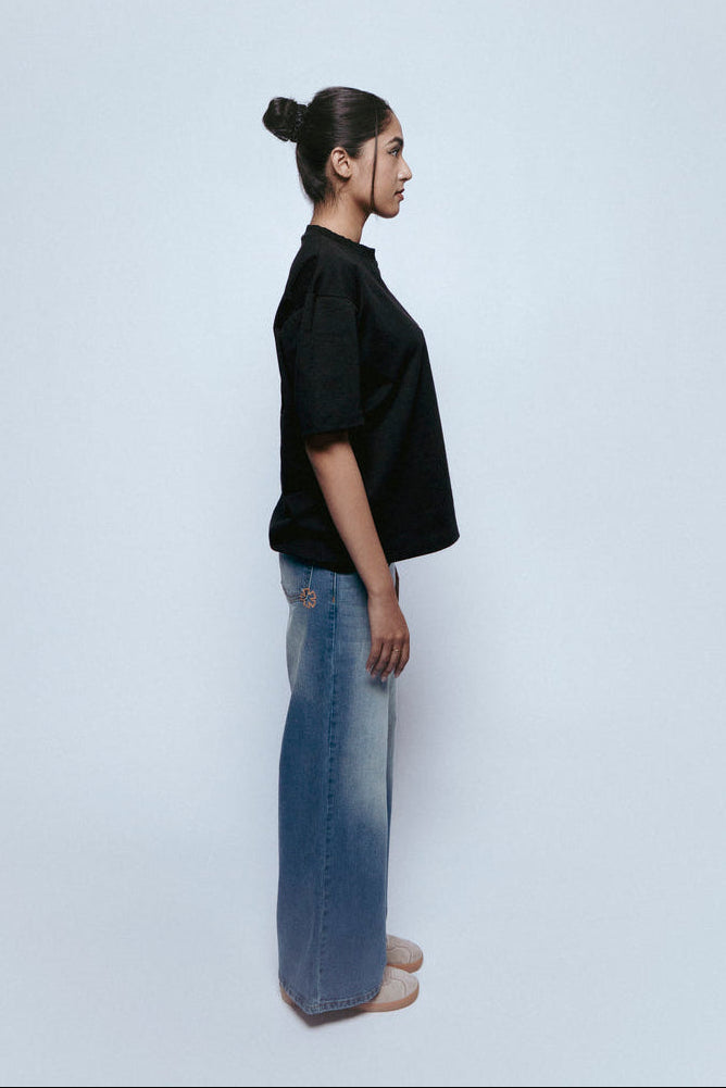 Person wearing a black SOH Mark T-shirt and SOH Morning Indigo jeans standing against a white background