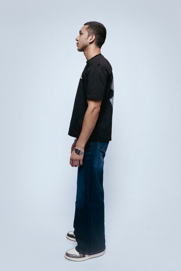 Person wearing a black SOH Mark T-shirtt and blue jeans standing against a white background