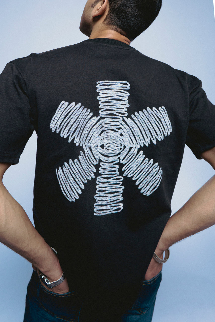 Person wearing a black SOH Mark T-shirt with a white abstract design on the back against a light blue background