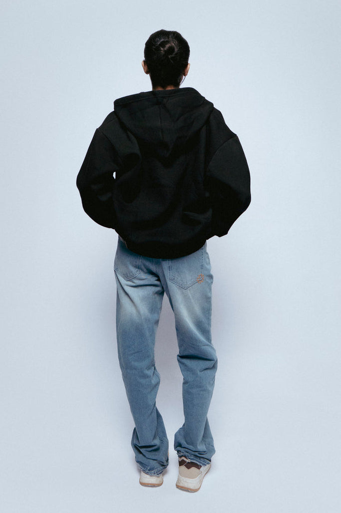 Person wearing a SOH Hoodie Error 01 and SOH Noir jeans standing against a white background