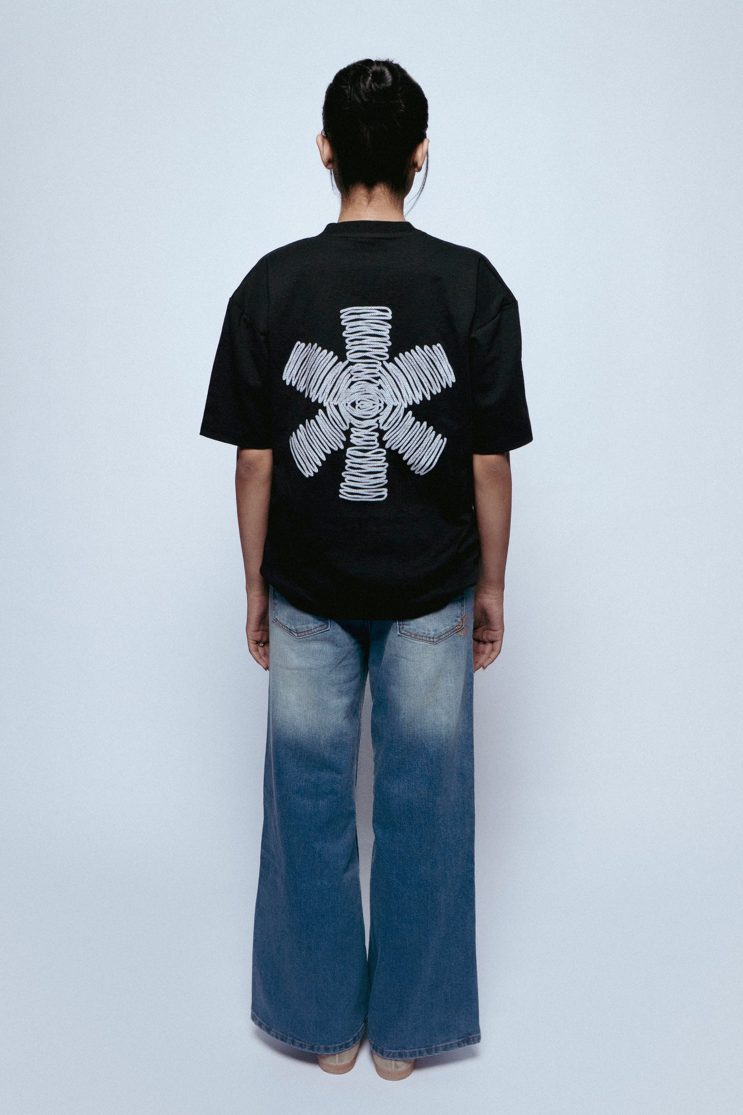 Person wearing a black SOH NOVA MARK t-shirt and SOH NOVA jeans with a white design on the back, standing against a plain white background.