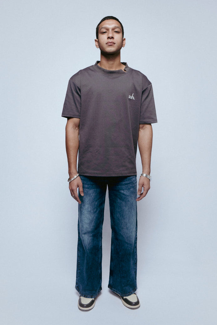 Man wearing a gray SOH Question T-shirt and blue jeans standing against a white background