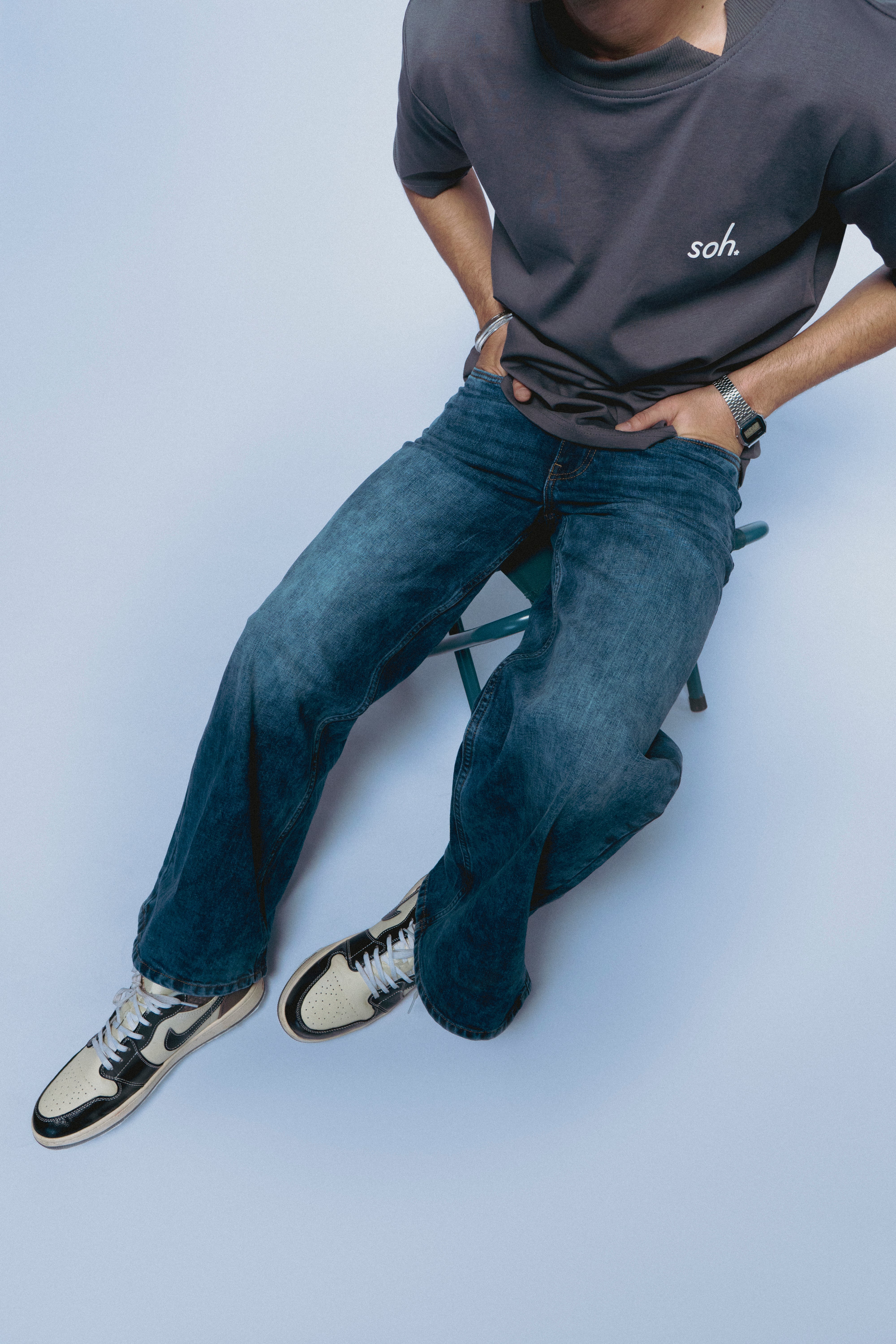 Person wearing a gray SOH Question T-shirt and blue jeans sitting on a chair against a light background