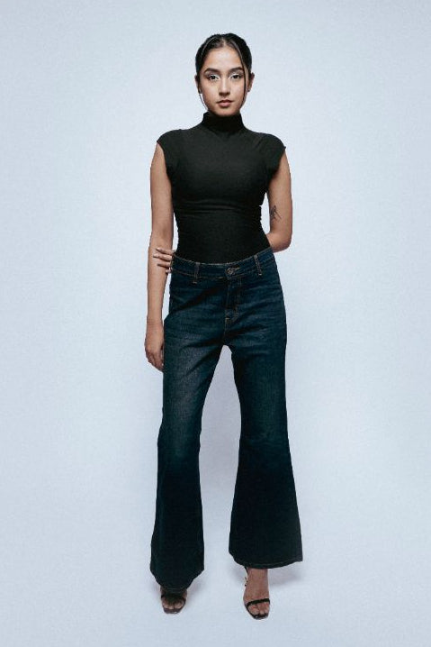 Person wearing a black turtleneck and Starlit Afterlight Indigo jeans on a light gray background