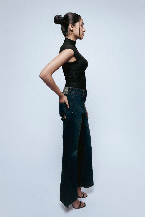 Woman wearing a black sleeveless top and Starlit Afterlight Indigo jeans standing against a light gray background